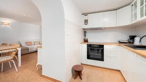 Uma cozinha compacta com armários brancos, forno embutido e um banquinho pequeno.
