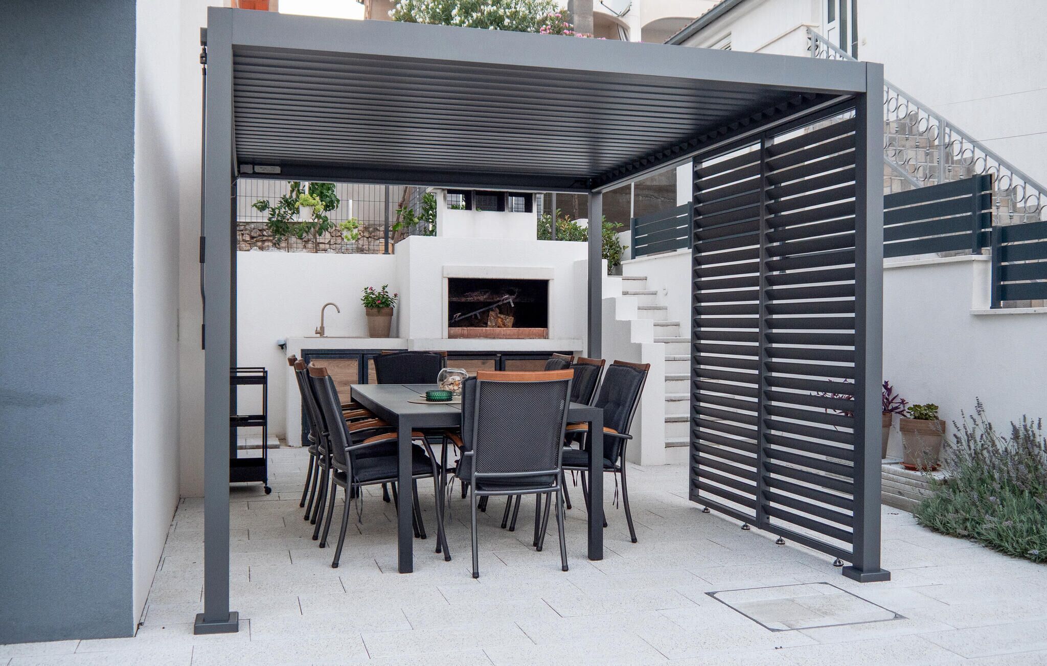 A patio with a table and chairs, a grill, and a white wall with a window.