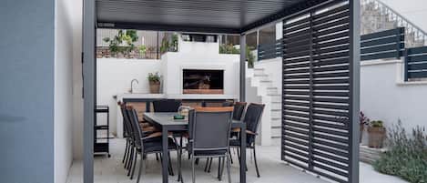Un patio con mesa y sillas, una parrilla y una pared blanca con una ventana.