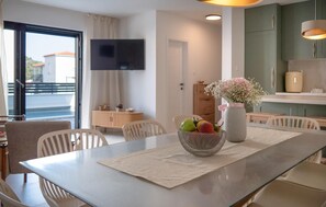 Ein moderner Essbereich mit einem Tisch für zwei Personen, einer Obstschale und einer Vase mit Blumen.