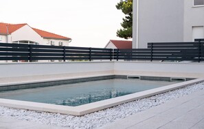 Ein rechteckiger Pool mit schwarzem Zaun, umgeben von weißen Kieselsteinen und einer gefliesten Terrasse.
