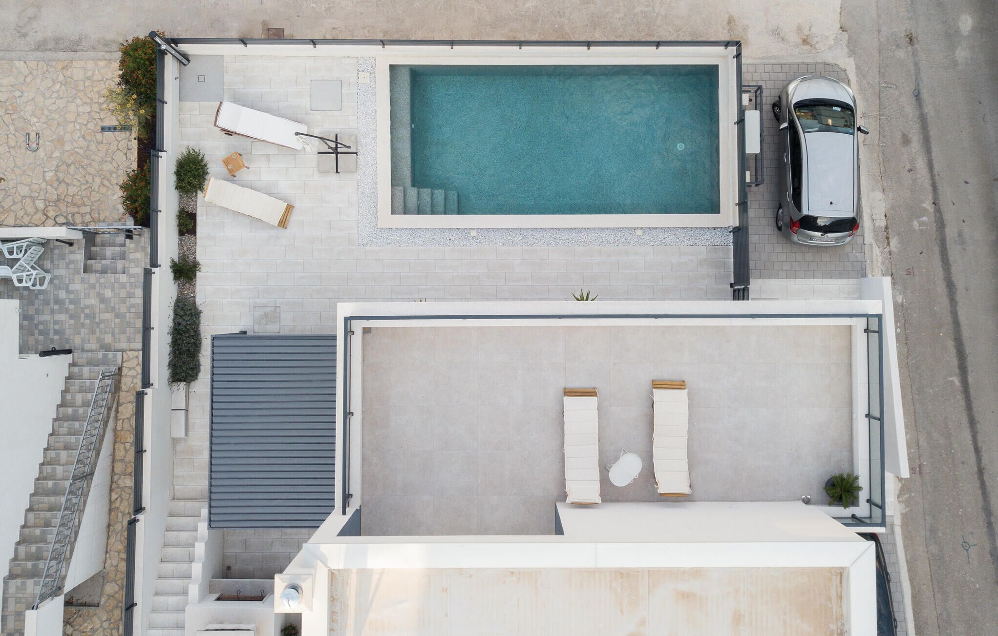 Vista aérea de una propiedad residencial con piscina, terraza cubierta y un coche estacionado en la calle.