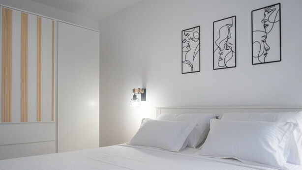 Ein Schlafzimmer mit einem Bett, weißer Bettwäsche, einer Wandleuchte und drei grafischen Bildern.