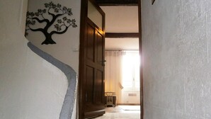 A hallway with a wooden door, a decorative tree wall art, and a tiled floor leading to a room with a window. - The perfect getaway on the square in Saint-Chinian, home to its famous wine (Saint-Chinian)