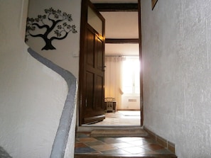 A hallway with a wooden door, a decorative tree wall art, and a tiled floor leading to a room with a window. - The perfect getaway on the square in Saint-Chinian, home to its famous wine (Saint-Chinian)