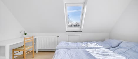 A bedroom with a sloped ceiling, a skylight, a radiator, a wooden chair, and a bed with striped bedding.