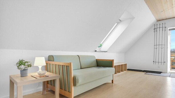 Ein modernes Schlafzimmer im Loft-Stil mit schrägem Dach, einer eingebauten Couch, einem Nachttisch mit Lampe und einer Topfpflanze.