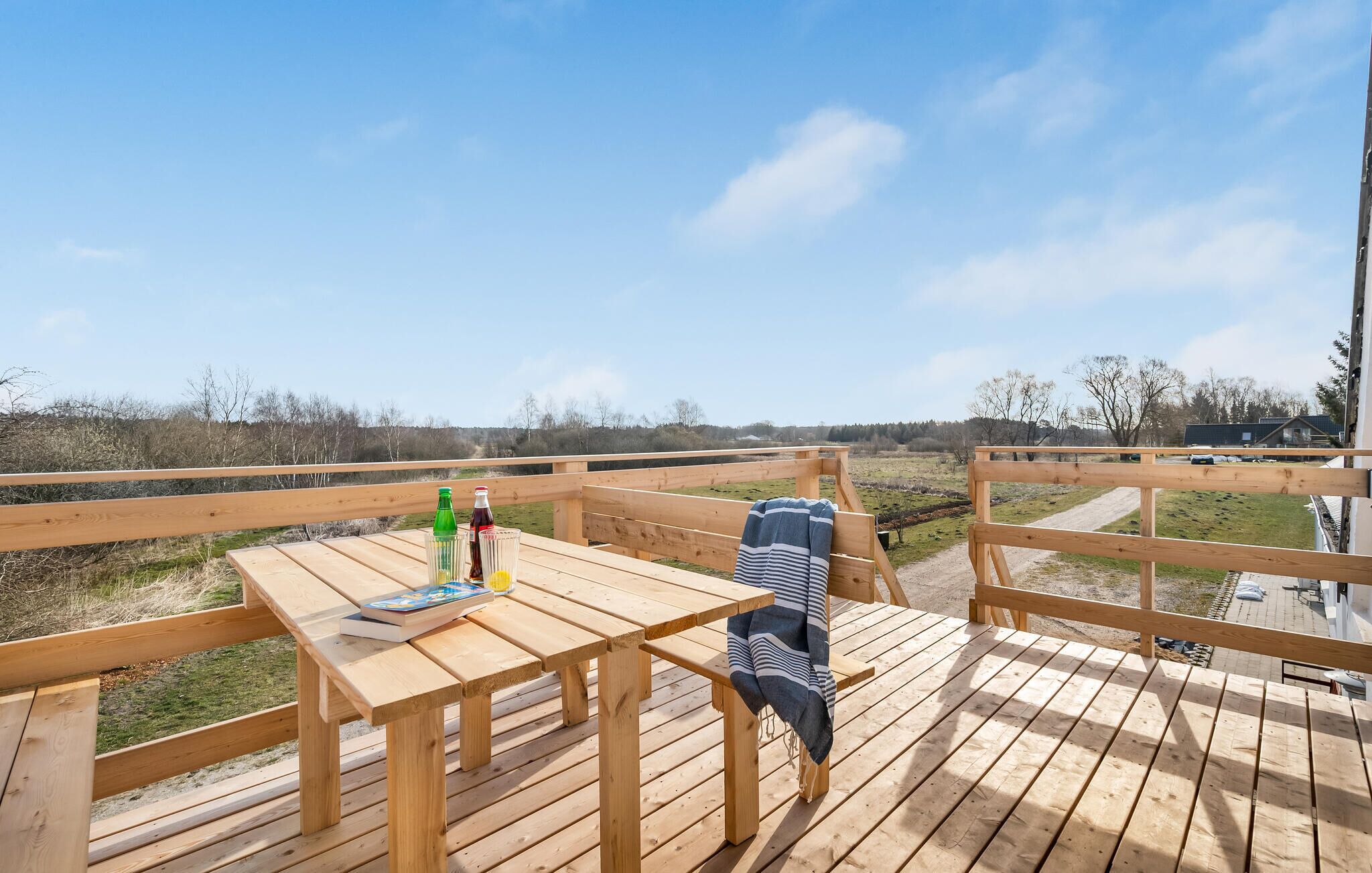 A wooden deck with a table, a bench, and a view of the countryside.