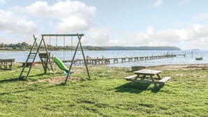 Ein Park mit Rasenfläche, einer Schaukel, einem Picknicktisch und einem Holzsteg, der sich über einen See erstreckt.