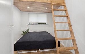 Ein kleines Zimmer mit einem Einzelbett, einer Holzleiter, einem Fenster mit Jalousien und einer kleinen Pflanze.