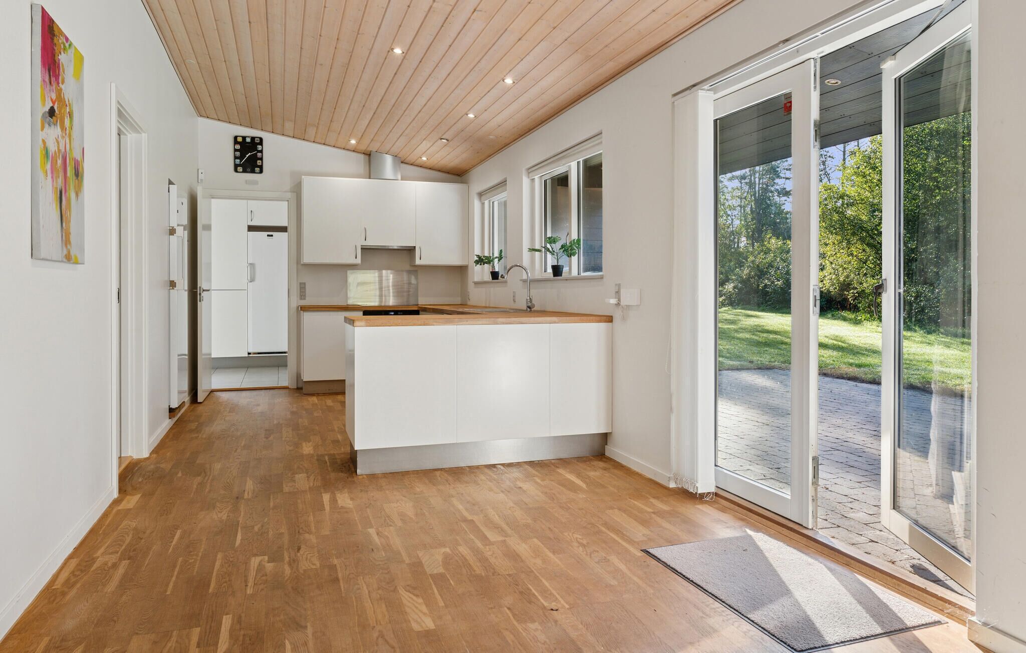 Eine moderne Küche mit Holzboden, weißen Schränken und einem großen Schiebeglasfenster zum Garten.