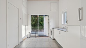 A modern kitchen with white cabinets, a built-in washing machine, and a view through an open door to a garden. - Awesome home in Bording with sauna (Bording)
