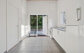 A modern kitchen with white cabinets, a built-in washing machine, and a view through an open door to a garden. - Awesome home in Bording with sauna (Bording)