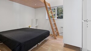 A bedroom with a bed, a white wardrobe, a wooden ladder, a white speaker, and a window with a view of trees. - Awesome home in Bording with sauna (Bording)