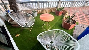 A balcony with artificial grass, two white wire chairs, a wooden table, and potted plants. - Beachfront 2-bedroom condo in La Libertad. (La Libertad)