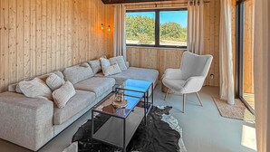 Una habitación con paneles de madera, un sofá, una silla, una mesa de centro de vidrio y vistas al exterior.