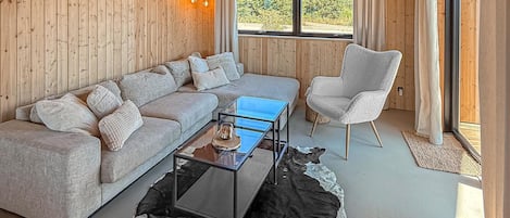 Um quarto com painéis de madeira, um sofá, uma poltrona, uma mesa de centro de vidro e vista para o exterior.