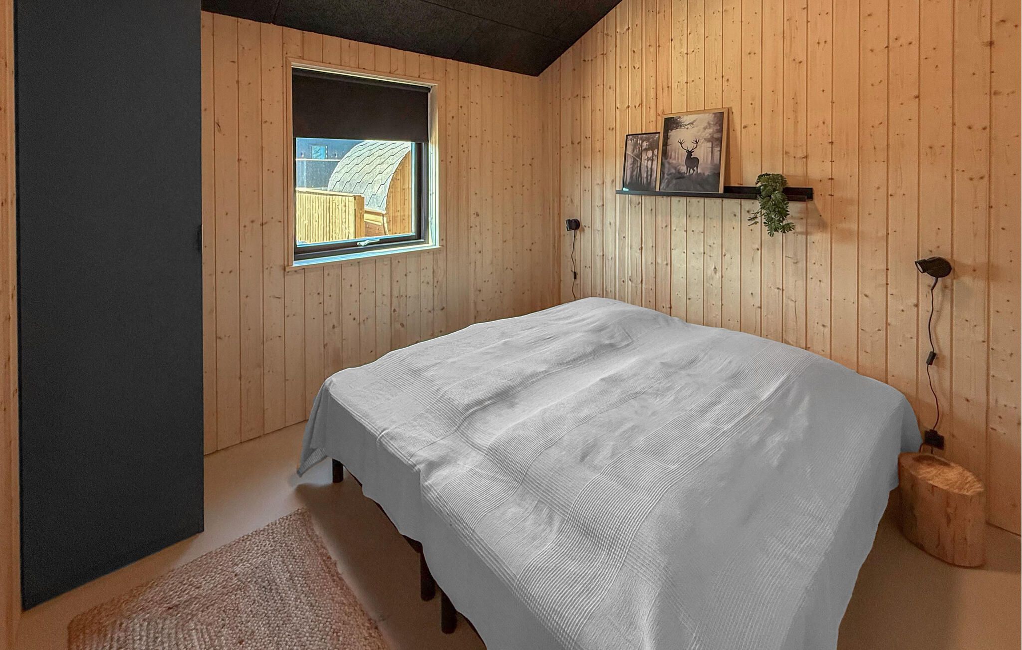 A bedroom with a bed, a window, and wooden walls.
