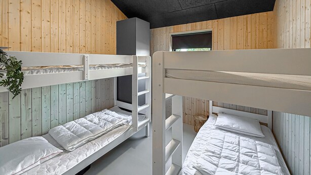 Camas literas con ropa de cama blanca, paredes de madera y una ventana.