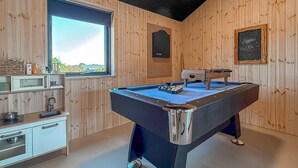 Una habitación con mesa de billar, ventana con vistas, pizarra con escritura y paredes de madera.