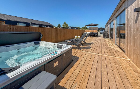 Eine Holzterrasse mit Whirlpool, Liegestühlen und einem überdachten Bereich.