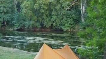 Une tente est installée sur l’herbe, près d’une étendue d’eau, et une chaise se trouve à proximité.