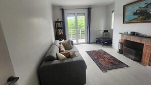 Een woonkamer met een bank, een open haard, een boekenkast en uitzicht door een glazen deur.