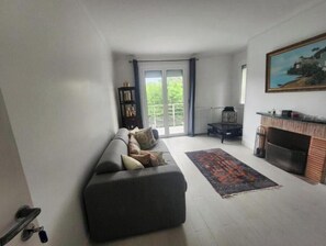 Ein Wohnzimmer mit Sofa, Kamin, Bücherregal und Blick durch eine Glastür.