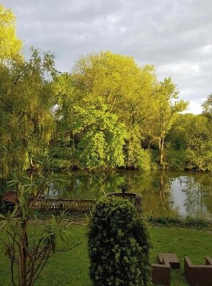 A serene garden with a pond, lush greenery, and a wooden deck. - Les Rives de Montigny-sur-Loing: 3-Bedroom Apartment (Montigny-sur-Loing)