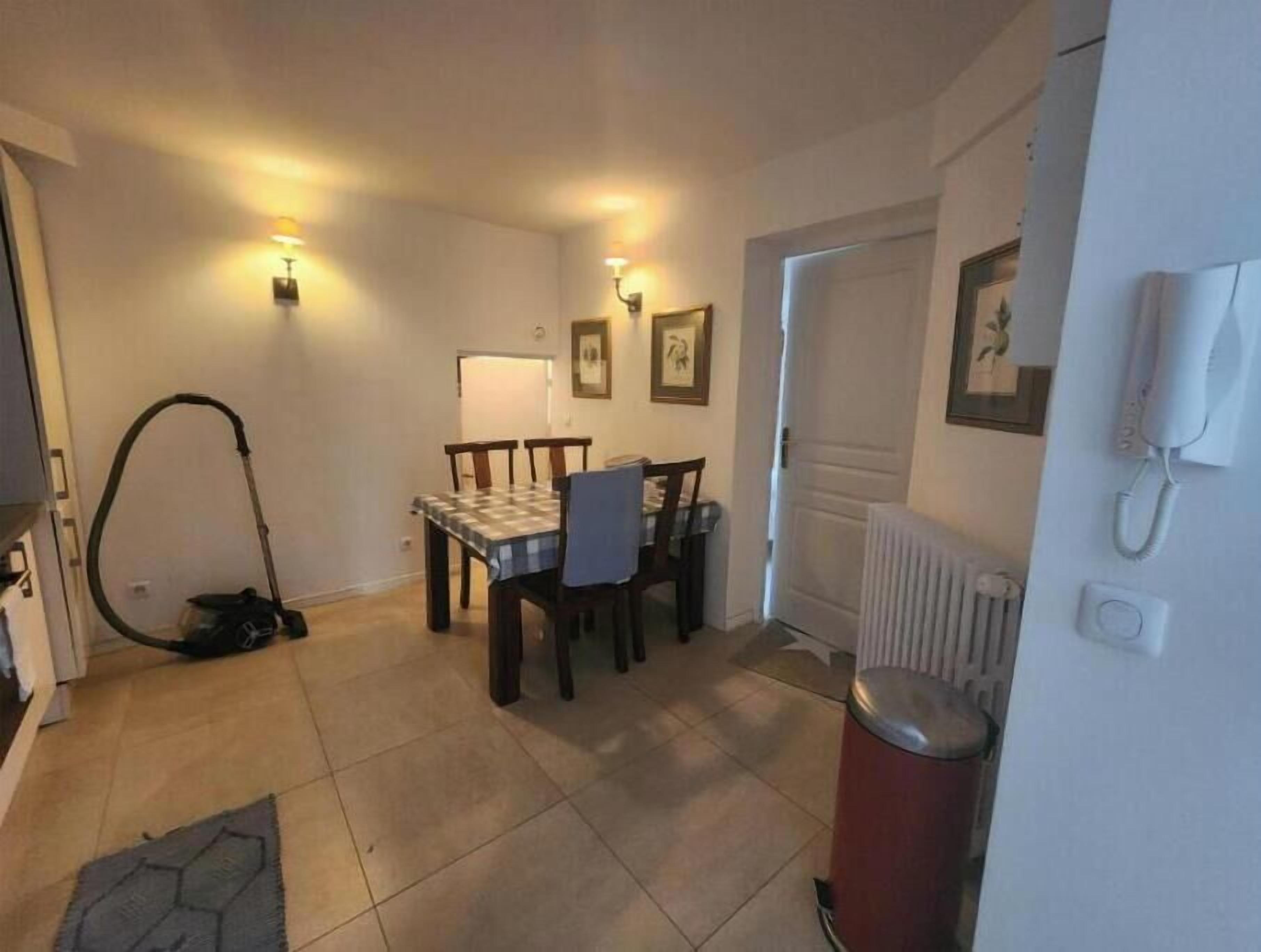 Un coin repas avec une table et des chaises, un aspirateur, un radiateur et une poubelle.