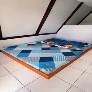 Ein Bett mit einem geometrisch gemusterten Überwurf, einem Holzkopfende und einem gefliesten Boden.