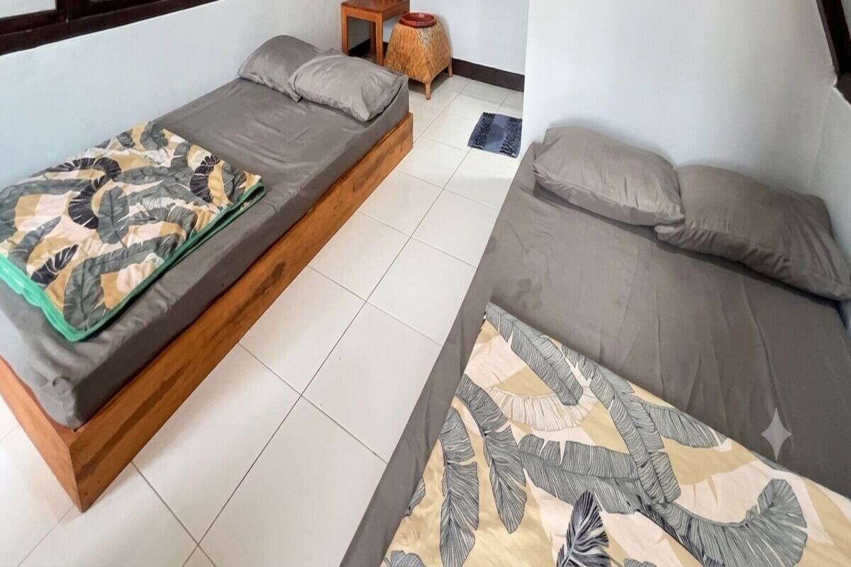 Ein Zimmer mit zwei Betten, einem kleinen Holztisch und einer gemusterten Tagesdecke.