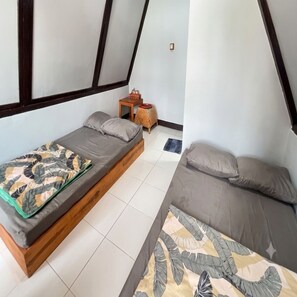 Ein Zimmer mit zwei Betten, einem kleinen Holztisch und einer gemusterten Tagesdecke.
