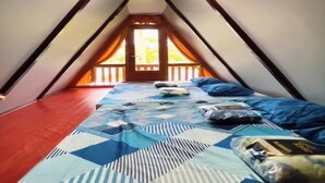 Un dormitorio bajo los tejados, con techo inclinado, cama con ropa de cama estampada y vista al exterior a través de una puerta.