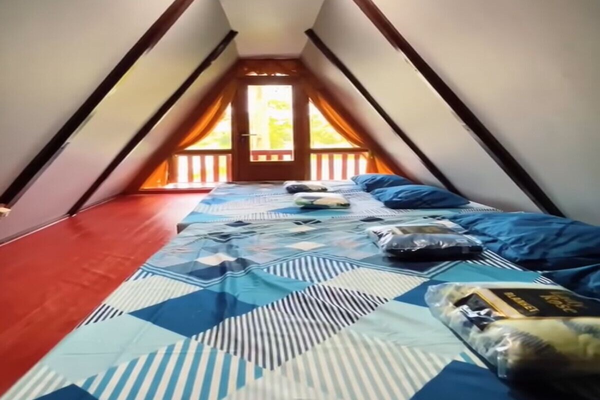 Ein schmales Schlafzimmer im Dachgeschoss mit schrägen Wänden, einem Bett mit gemusterten Textilien und Blick durch eine Tür nach draußen.
