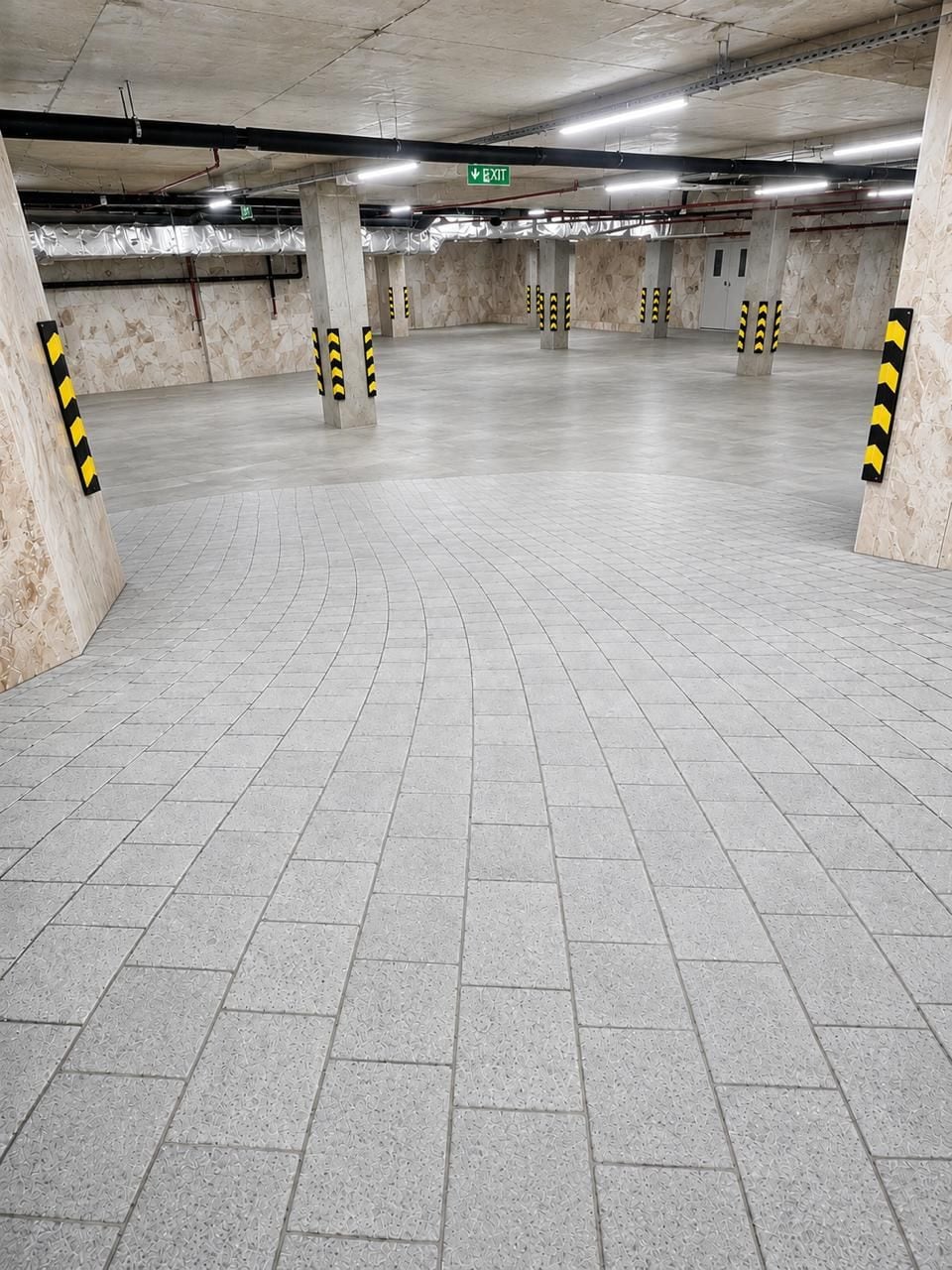 An underground parking garage with concrete pillars, a tiled floor, and an exit sign.