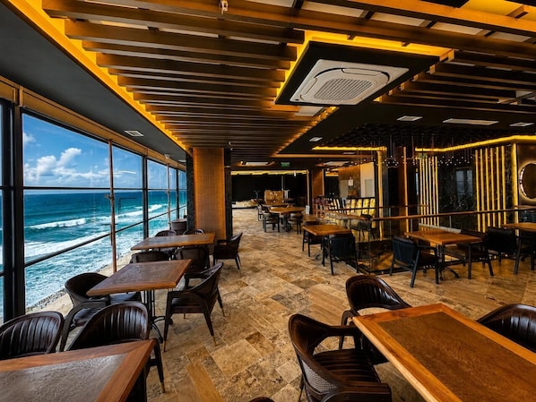 A restaurant with tables and chairs, a view of the ocean, and a modern interior design. - The New Jai Son (Kobuleti)