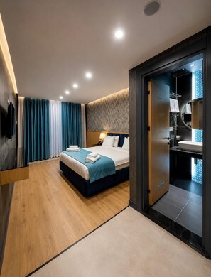 A modern hotel room with a large bed, a wooden floor, a bathroom with a sink and mirror, and a view of the city.