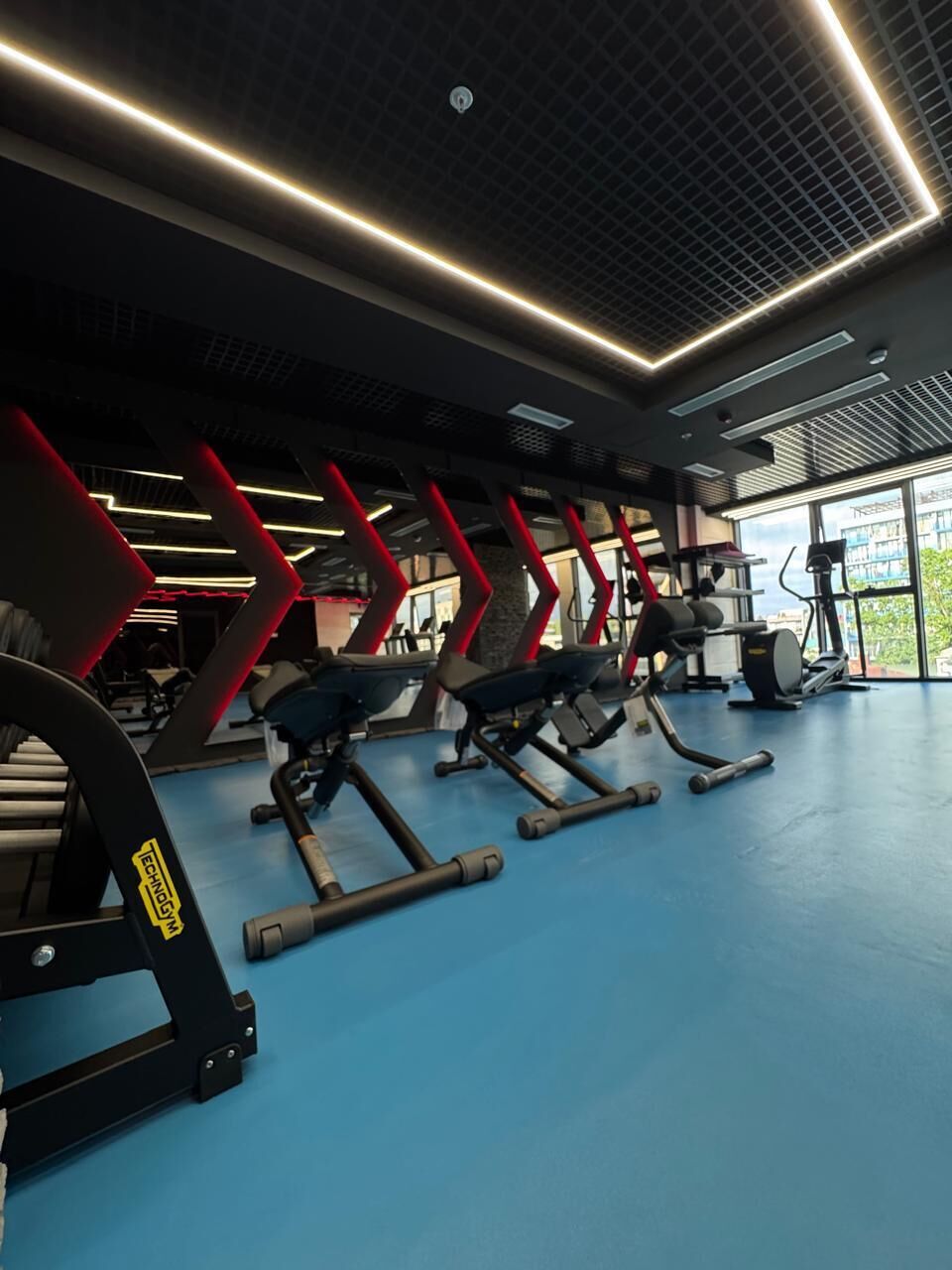 Un gimnasio con equipo de ejercicio, piso azul y techo con diseño de cuadrícula.