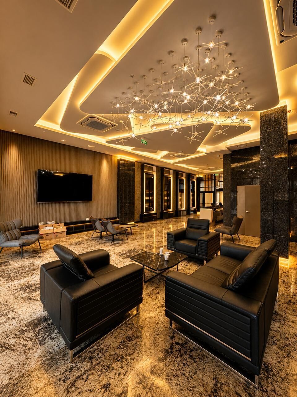 Um hall de hotel moderno com uma grande televisão de tela plana, assentos confortáveis e um luminário de teto exclusivo.