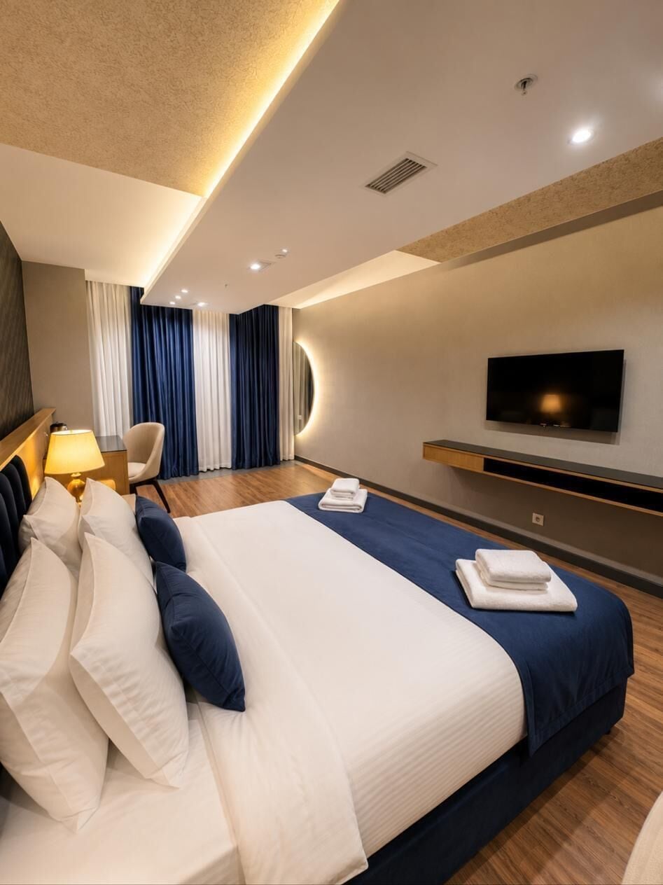 Una habitación de hotel moderna con una cama grande, un televisor de pantalla plana montado en la pared, un escritorio con lámpara y una silla.