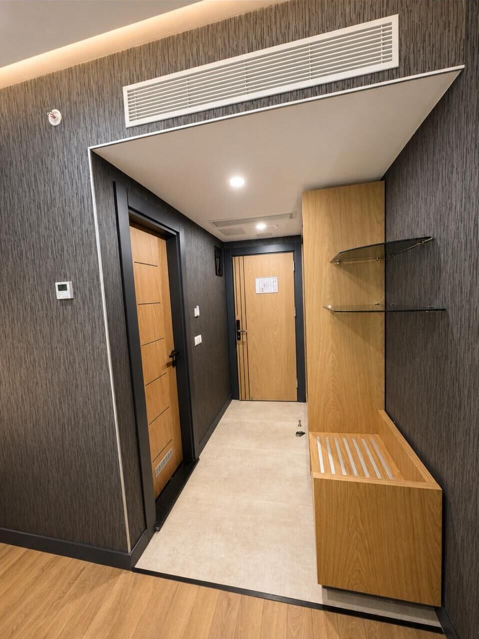 A hallway with a wooden door, a ventilation system, and a small shelf unit.