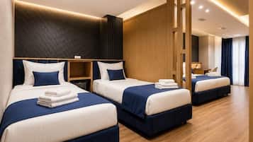 Quarto de hotel com três camas, piso de madeira e design moderno.