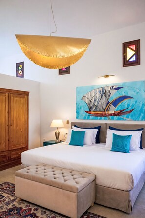 Ein Schlafzimmer mit einem Bett, einem geschnürten Ottomanen, einem großen abstrakten Gemälde, einem Holzschrank und einer Hängeleuchte.