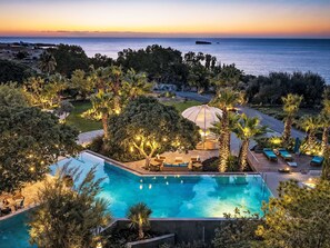 Ein Pool mit einer Liegeinsel, umgeben von Bäumen und Blick auf das Meer bei Sonnenuntergang.