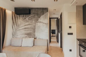 Ein modernes Schlafzimmer mit einem großen Bett, einem an der Wand befestigten Fernseher und einem zur Küche hin führenden Flur.