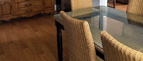 Un comedor con mesa de vidrio y sillas de mimbre, un aparador de madera, una lámpara y un ventilador de techo.