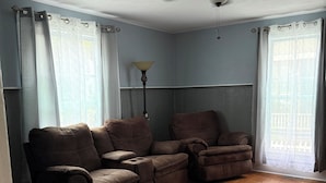 Un salon avec un ventilateur de plafond, un ensemble de canapés et une lampe.