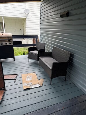 An outdoor patio area with a grill, wicker furniture, and a partially visible house. - Charming 4-bedroom house in Warren perfect for your getaway (Warren)