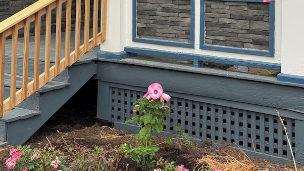 Une maison avec une façade en pierre, un escalier en bois et un porche orné d’un drapeau américain et d’une bannière.
